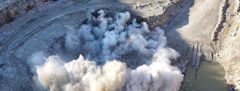 landscape_explosion Aerial view of a quarry during a large explosion. Rocky terrain appears rugged and barren.
