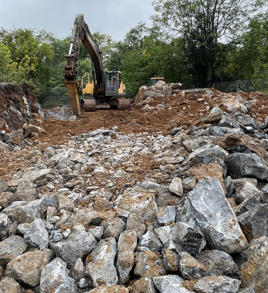 mechanical-drilling-rocks Large drilling equipment onsite digging into large stones and gravel
