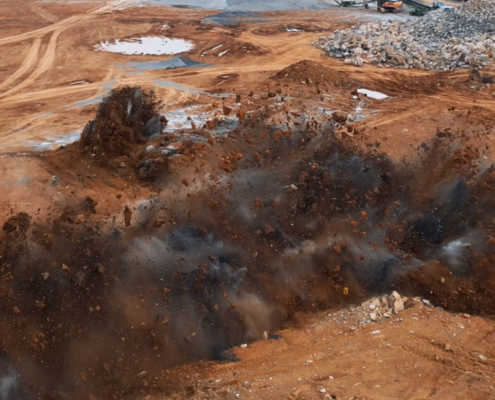 screenshot-explosion A construction site explosion sends dirt and debris into the air, with nearby equipment and piles of gravel in the background, capturing a sense of power and activity.