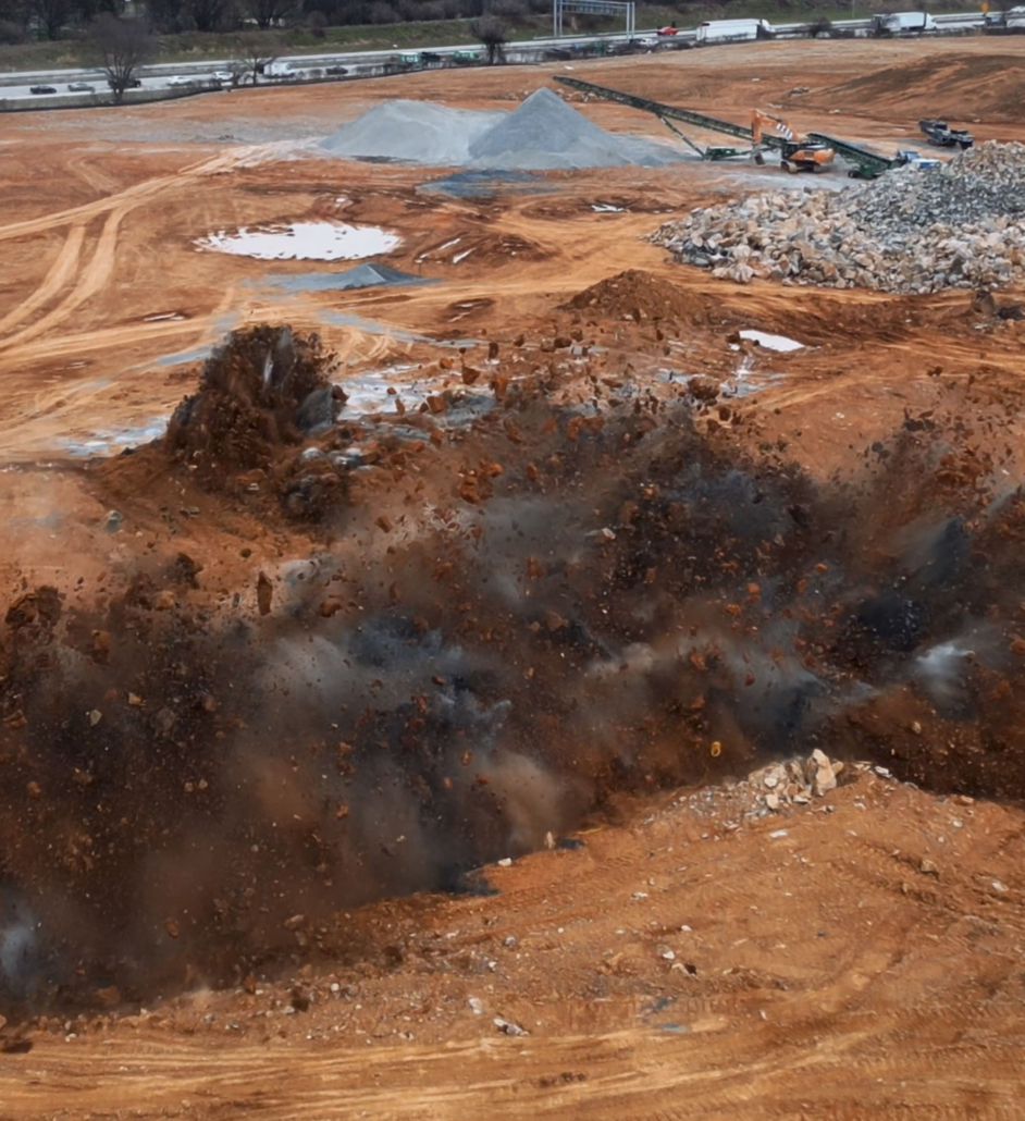 screenshot-explosion A construction site explosion sends dirt and debris into the air, with nearby equipment and piles of gravel in the background, capturing a sense of power and activity.